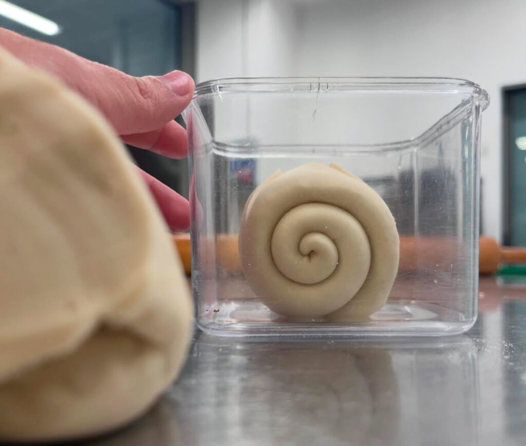 Mani al lavoro sull’impasto, pasta madre arrotolata in vaschetta
